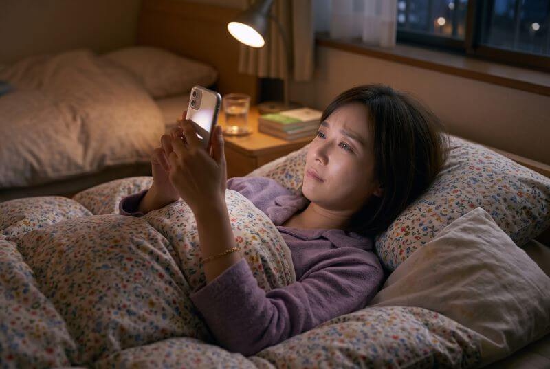 布団の中でスマートフォンを見ている女性